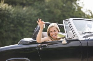 A young woman sitting in a black sports car holding the keys